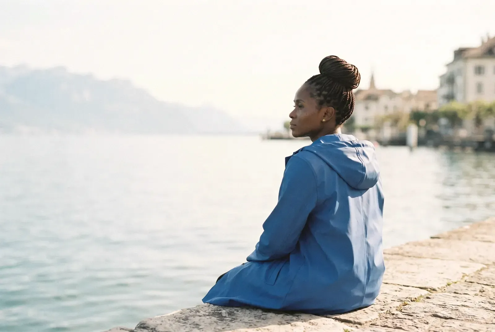 Une femme en veste bleue assise sur un quai au bord du lac, face aux montagnes